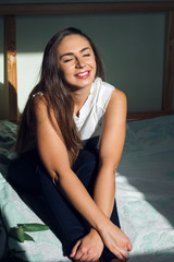 beautiful caucasian woman sitting on the bed and smiling in the sun light