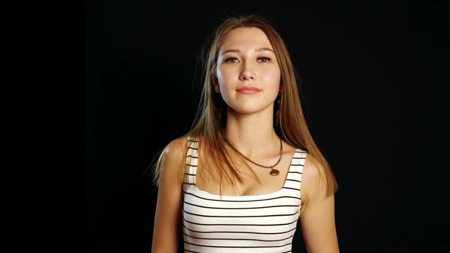 A cute young white girl straightens hair, looking on camera on black background