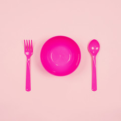 Set of empty pink plastic tableware bowls, spoons and forks isolated on pink pastel background. Flat lay, Top view. Minimal style.
