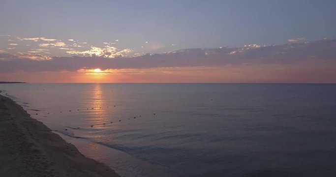 Dawn. Two women run in the surf. The cattery flies over the beach and flies over the sea but the morning sun. It shines through the pink clouds.