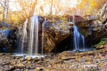A  small waterfall in the mountains among the autumn forest. Golden autumn.