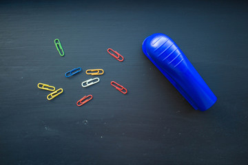 a stepler and colored clips on black background