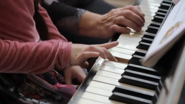 little baby girl sitting on the teacher lap, playing the piano