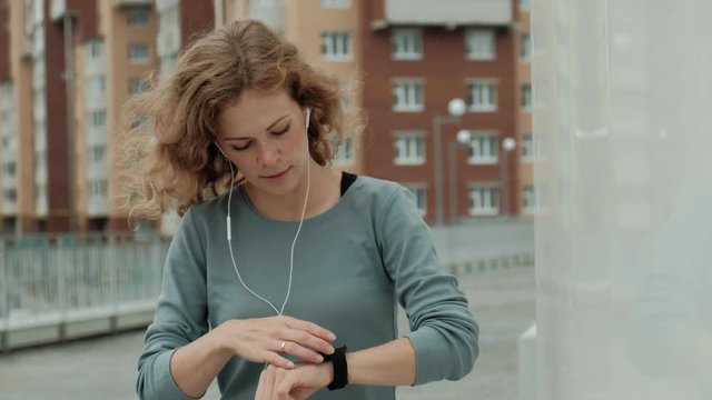 Pretty smiling fitness woman using running app before the run for track the pace on smartwatch, happy smiling sportive girl texting message on smartphone before morning workout