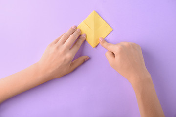 Woman making origami boat on color background