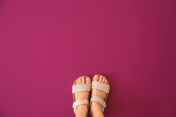 Legs of girl wearing sandals on color background
