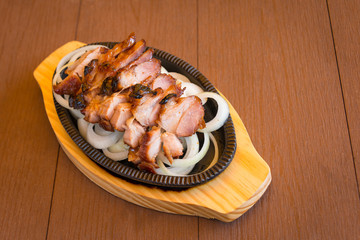 Roasted pork slices in a hot pan with onion on wooden board the favorite delicious food of Thailand
