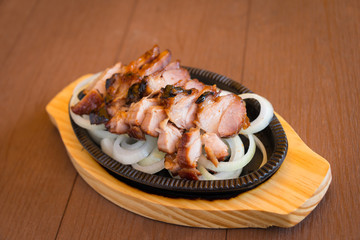 Roasted pork slices in a hot pan with onion on wooden board the favorite delicious food of Thailand
