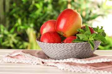 Bowl with ripe fresh apples and mint on light wooden table