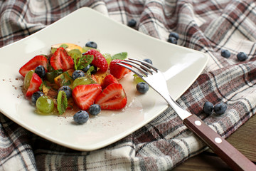 Plate with delicious fruit salad on table