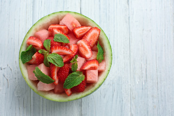 Delicious fruit salad in melon bowl on light wooden table