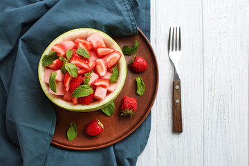Delicious fruit salad in melon bowl on light wooden table