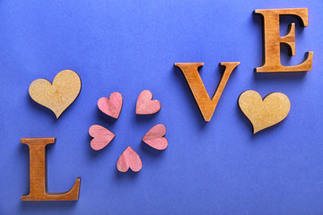 Word LOVE made of wooden letters and hearts on color background