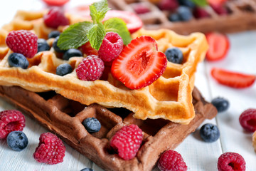 Delicious waffles with berries on white wooden table