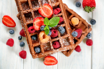 Delicious waffles with berries on white wooden table