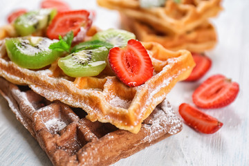 Delicious waffles with kiwi slices and strawberry on white wooden table