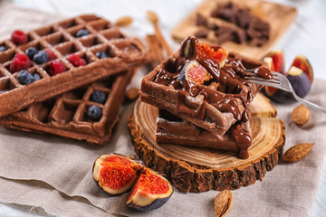 Delicious waffles with fig slices and chocolate sauce on wooden board