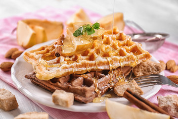 Pouring of honey onto delicious waffles with pear slices on plate