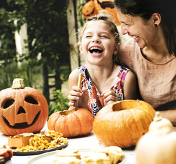 Young cheerful girl carving pumpkins with her mom