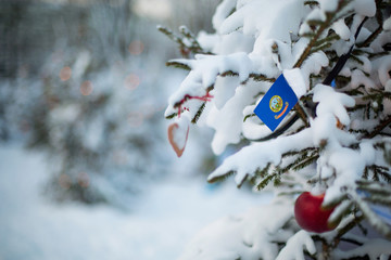 Idaho state flag. Christmas background outdoor. Christmas tree covered with snow and decorations and Idaho flag.  New Year / Christmas holiday greeting card.