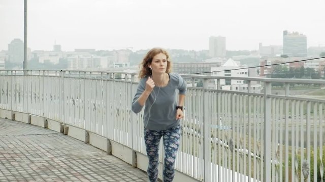 Pretty smiling fitness woman using running app before the run for track the pace on smartwatch, happy smiling sportive girl texting message on smartphone before morning workout