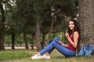 Naklejka na ściany i meble Beautiful young woman listening to music near tree in park