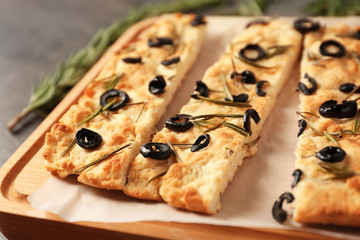 Traditional Italian Focaccia with rosemary and olives on wooden board, closeup