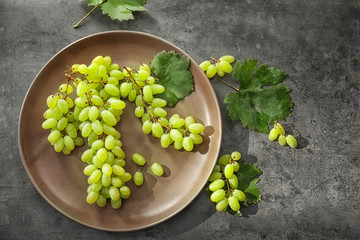 Plate with ripe juicy grapes on grey table