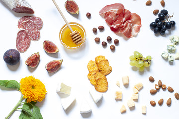 Antipasti food white flat lay with nuts, honey, cured meat, salami, cheeses, grapes and figs. Top view snack concept composition