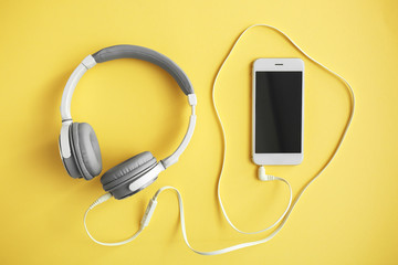 Headphones with mobile phone on color background