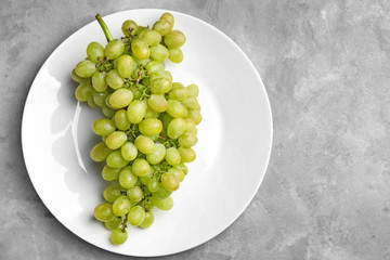 Plate with ripe juicy grapes on grey table