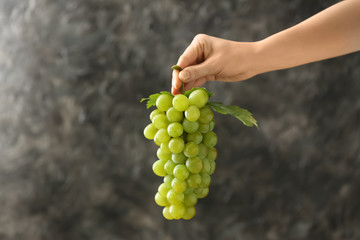 Female hand holding ripe juicy grapes on grey background