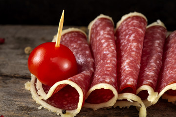 Slices of salami surrounded by parmesan cheese with peppercorns and cherry tomato