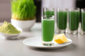 Glass of fresh wheat grass juice with lemon on table