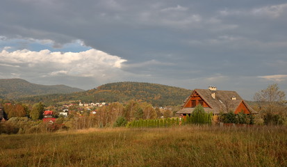 Mountain, rural autumnal landscape with traditional house (cottage), hills, meadow, trees, cloudy sky.