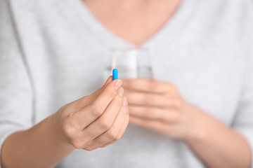Woman holding pill and glass of water, closeup