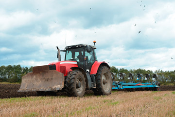 Red tractor plowing the ground. Farmer working in field. Cultivation of land. Agricultural machine