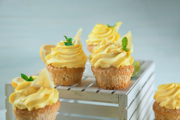 Delicious lemon cupcakes and white wooden crate on light background