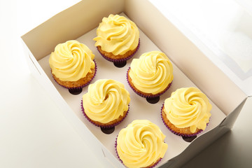 Box with delicious lemon cupcakes on white background