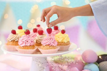 Woman decorating delicious cupcakes with raspberry at table