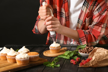 Woman decorating delicious cupcake with cream at table