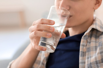 Young man drinking water at home, closeup