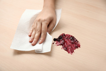 Woman wiping spot of jam on wooden table with paper towel