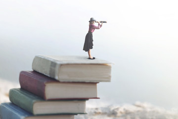 miniature woman looks at the infinity with the spyglass on a scale of books