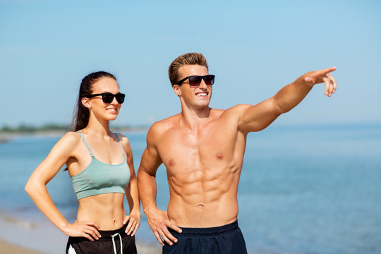 fitness, sport and lifestyle concept - happy couple in sports clothes and sunglasses on beach