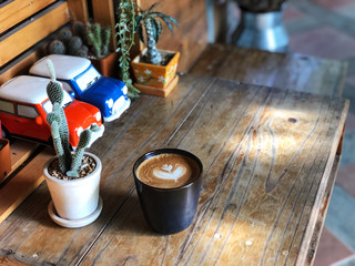 Cup of love ,Love heart latte art coffee in Black cup and mini Cactus  on the wooden table With  Vintage background ,wake up and full fill energy. 
