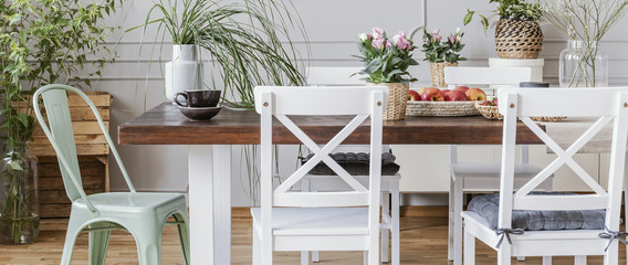 Panorama of chairs at wooden table with flowers in rustic dining room interior with plants. Real photo