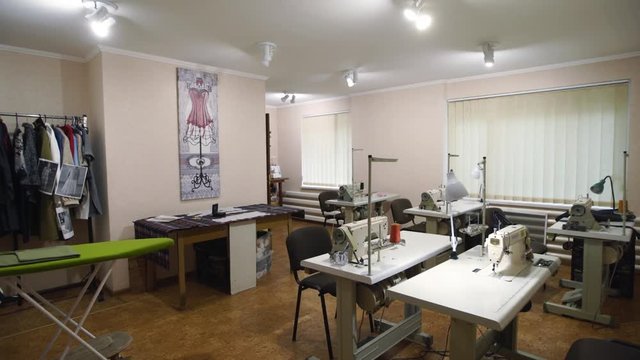 Empty designer atelier interior with tables and sewing machines. Equipped fashion tailoring studio indoors with clothes and reels of threads, no people.