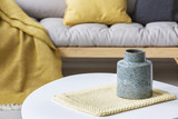 Close-up on grey vase on pad on round table in modern living room interior with yellow. Real photo