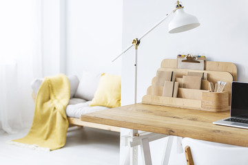 White lamp on wooden desk with laptop in bright freelancer's interior with organizer. Real photo